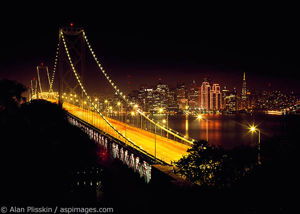 The lights of San Francisco glow across the Bay beyond the Oakland Bay Bridge.