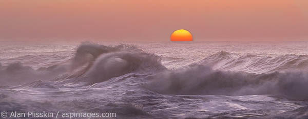 The sun sets in the Pacific Ocean past the wavebreaks at Ke'e Beach.